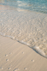 Minimal, people-free close-up of a gentle wave with foam over smooth sand and clear shallow water on the Ionian coast in Ksamil, Albania—versatile for travel, wellness and resort branding, with copy s