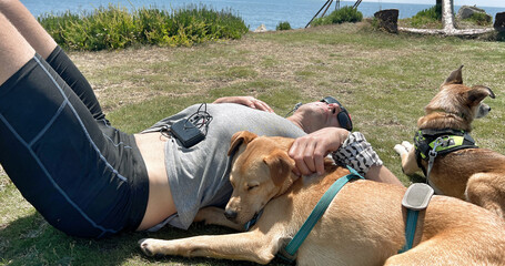 A fit slim man lying with dogs, sleeping & relaxing in a field on a sunny day in lycra shorts