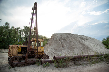 An old pipelayer against the backdrop of pipe sections and a pile of sand washed up by a dredger