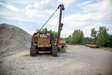 An old pipelayer against the backdrop of pipe sections and a pile of sand washed up by a dredger