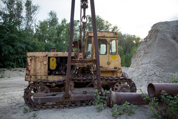 An old pipelayer against the backdrop of pipe sections and a pile of sand washed up by a dredger