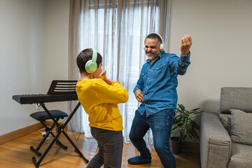 Father and son dancing joyfully at home, wearing headphones and sharing a fun moment filled with music and laughter together
