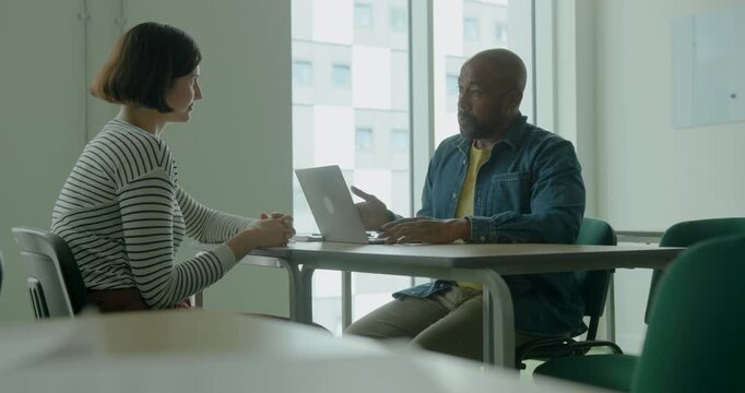 Teacher Talking to Student in Classroom, using Laptop to review performance