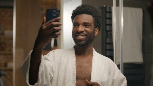 African American man blogger model influencer selfie photo mobile phone in bathroom skincare blog vlog social media handsome smiling ethnic male guy posing at home bath face cosmetics video smartphone