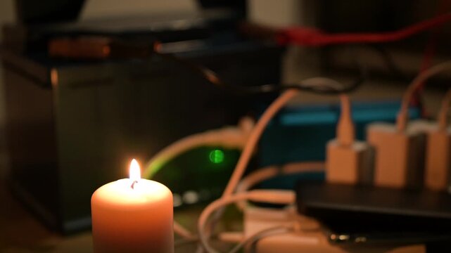 Charging gadgets during a blackout by candlelight. A burning candle, against the background of which gadgets are charged from a car battery as the only source of electricity during a power outage
