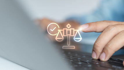 Close-up hand using a laptop with a digital justice balance icon and check mark. Concept for business compliance, law, ethics, legal technology, and corporate governance.