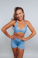 Fototapeta premium Smiling woman poses in blue athletic outfit against a neutral background in a studio setting