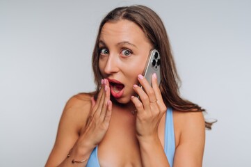Surprised woman talking on the phone while showing excitement and curiosity in a simple background...