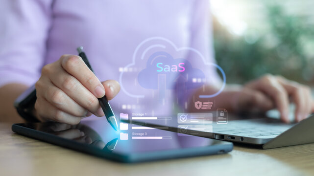Business person using tablet and laptop with SaaS cloud computing icon for digital data storage, online service, and modern software as a service technology concept.