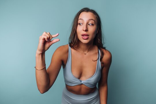 Young woman demonstrating a small size with fingers against a solid blue background