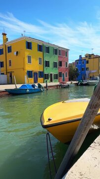 Colorful architecture in Burano island, Venice, Italy. Yellow and blue boats on the canal. Green and yellow houses in the background. Famous travel destination. Vertical video
