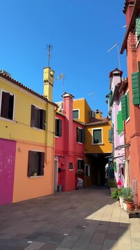 Colorful architecture in Burano island, Venice, Italy. Pink, yellow, red and blue colorful painted houses against the blue sky. Famous travel destination. Vertical video
