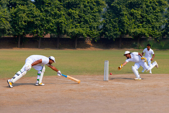 A wicketkeeper dives to catch the ball as a batsman attempts to make his ground on a cricket field
