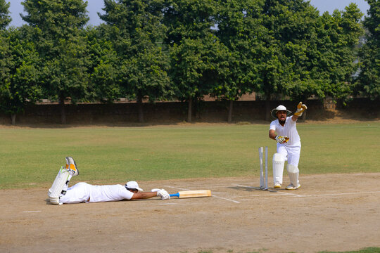 A wicketkeeper in white appeals for a run-out, as a batsman dives to make his ground on a cricket field