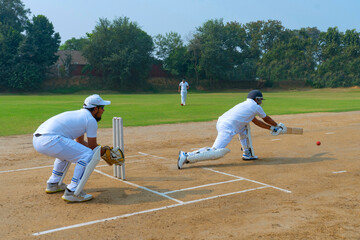A batsman in white uniform playing a precise shot on a cricket field, with a wicketkeeper and fielder in view
