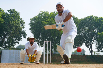 A cricketer hitting the ball with precision on a cricket pitch, with a wicketkeeper ready behind the stumps
