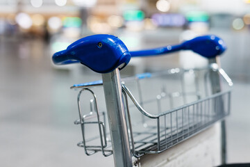Shopping cart with unique blue handle design, positioned in a spacious airport terminal, showcasing modern travel convenience and consumer experience in a bustling environment © wedmoments.stock