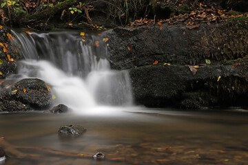 Scaleber Force Waterfall over black rocks and fallen colorful leaves.