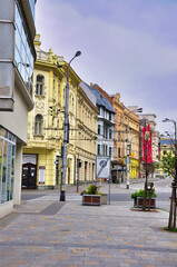 Osrtava - Tętniąca życiem ulica z pastelowymi fasadami, dekoracyjną architekturą i strefą dla pieszych wzdłuż brukowanego chodnika.