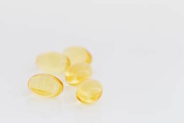 Close-up of several fish oil Omega-3 gel capsules on light background. Yellow transparent capsules viewed from the front. Shallow depth of field, focused on the foreground. Copy space.