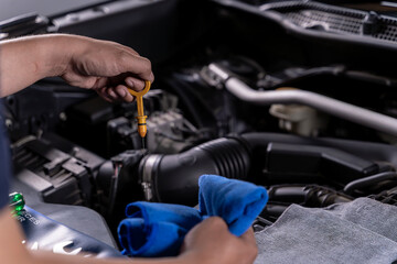 Fototapeta premium Young man inspecting the engine oil level of his car for regular maintenance and vehicle safety