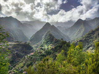 Idyllic view of green, foggy mountains, winding road and small village. Exotic and tranquil landscape of Madeira island, Portugal