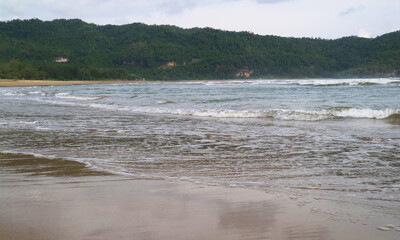 Sandy beach with rolling waves and a verdant hill. Calm ocean, lush nature, and peaceful landscape.