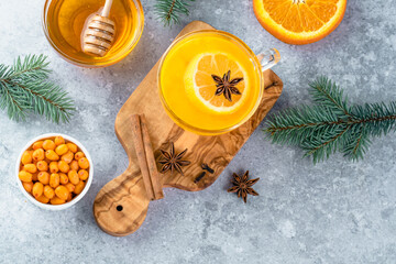 A cup of sea buckthorn tea with orange, cloves, honey, cinnamon, star anise, honey on a cutting board decorated with Christmas tree branches. Healthy herbal autumn drink well-being. top view