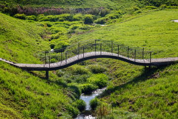 A curved bridge over a stream against a background of green grass on a clear sunny day. Architecture of World tourism.