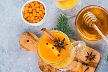  Close up a cup of sea buckthorn tea with orange, cloves, honey, cinnamon, star anise, honey on a cutting board decorated with Christmas tree branches. Healthy herbal autumn drink well-being. top view