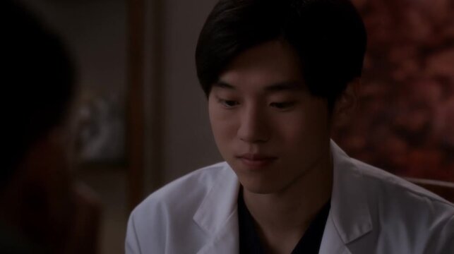 A young Asian man in a white coat paying attention