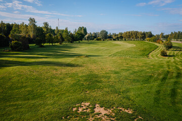 Sunny day at a green golf course with clear skies, manicured fairway, and tee-off area surrounded by trees at Avoti Golf Course, Latvia.