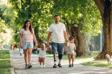 Fototapeta premium Smiling, enjoying the walk. Family of father that is amputee with prosthesis, mother and two kids