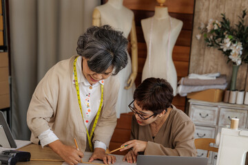 two Asian women collaborating in a clothing design studio.