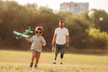 Active, running with toy plane. The amputee father is with his son on the field
