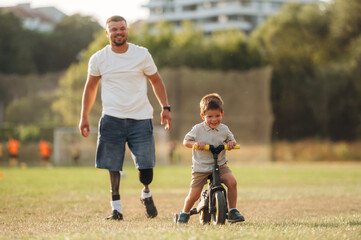 Teaching how to ride a bicycle. The amputee father is with his son on the field
