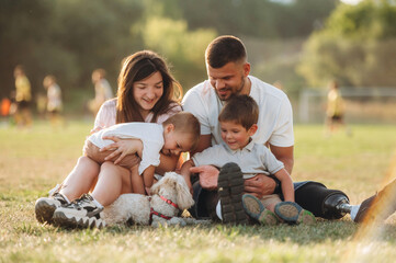 Fototapeta premium Resting by sitting on the ground. Mother, amputee father with prosthesis and kids are on the field