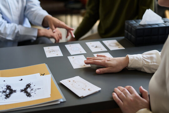 Middle aged woman conducting psychological assessment using inkblot test cards and diagrams on desk while discussing results with two people during therapy session