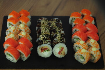Sushi set on black stone plate, assorted Japanese rolls with salmon, tobiko, cream cheese, cucumber, sesame and sauce, traditional Asian cuisine