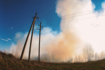 Rural field burning with thick smoke, under a blue sky, framed by strong utility poles.