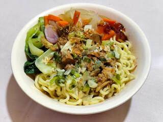 A bowl of delicious chicken noodles, complete with claws, dumplings, chicken pieces on top, traditional Indonesian food.