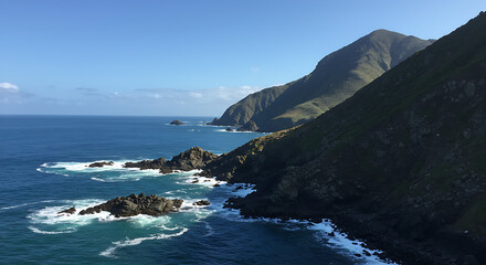 Spectacular view of rugged cliffs and rocky coastline with crashing waves under a clear blue sky.