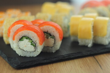 Sushi set on black stone plate, assorted Japanese rolls with salmon, tobiko, cream cheese, cucumber, sesame and sauce, traditional Asian cuisine