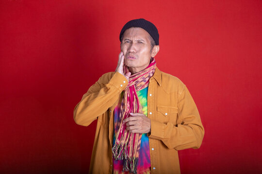 Dental Distress: Senior Man in Retro Outfit Expressing Toothache Pain Against a Vivid Red Background