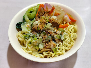 A bowl of delicious chicken noodles, complete with claws, dumplings, chicken pieces on top, traditional Indonesian food.