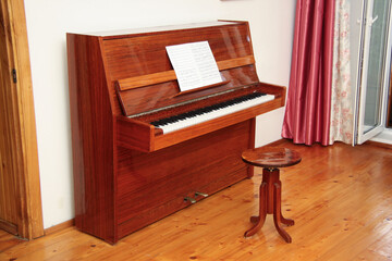 Classic Wooden Upright Piano with Sheet Music on Stand in a Bright Room with Curtains and Hardwood Floor