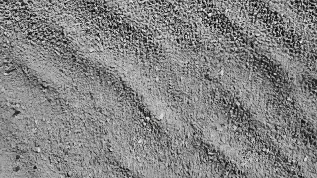 Overhead view of a granular surface with numerous small grey and white pebbles and faint parallel marks across it