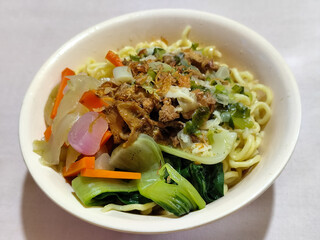 A bowl of delicious chicken noodles, complete with claws, dumplings, chicken pieces on top, traditional Indonesian food.
