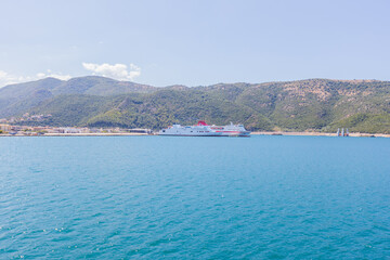 White passenger ferry docked at scenic Mediterranean port with crystal blue waters and mountains