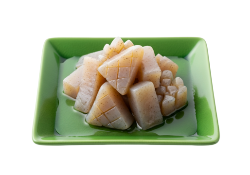 A close-up view of a pile of light beige konjac cubes on a glossy, vibrant green square plate, showcasing their intricate patterned shapes.